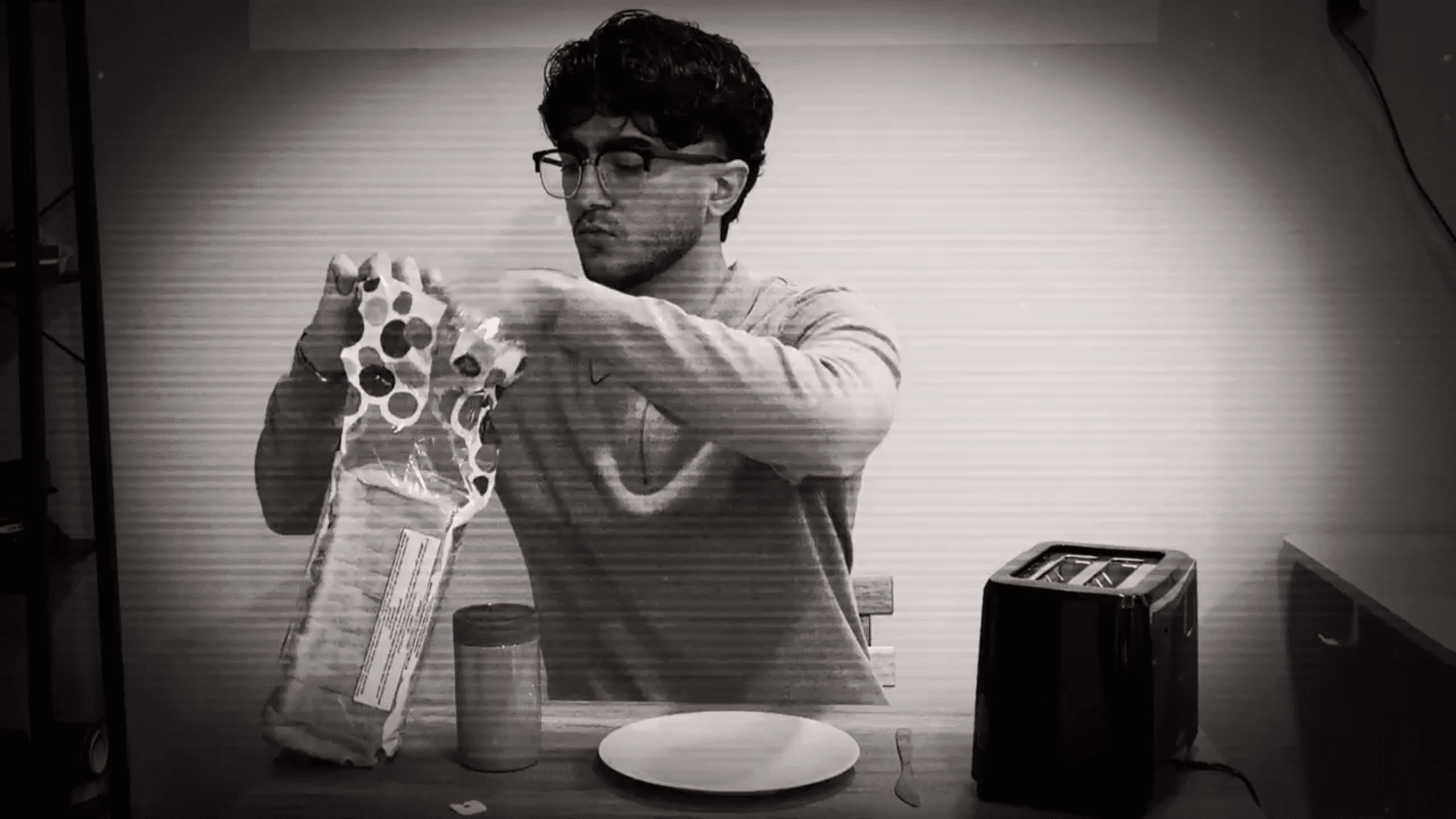 Black-and-white still of Radin opening a bag of bread at a kitchen table, from the Jam application film