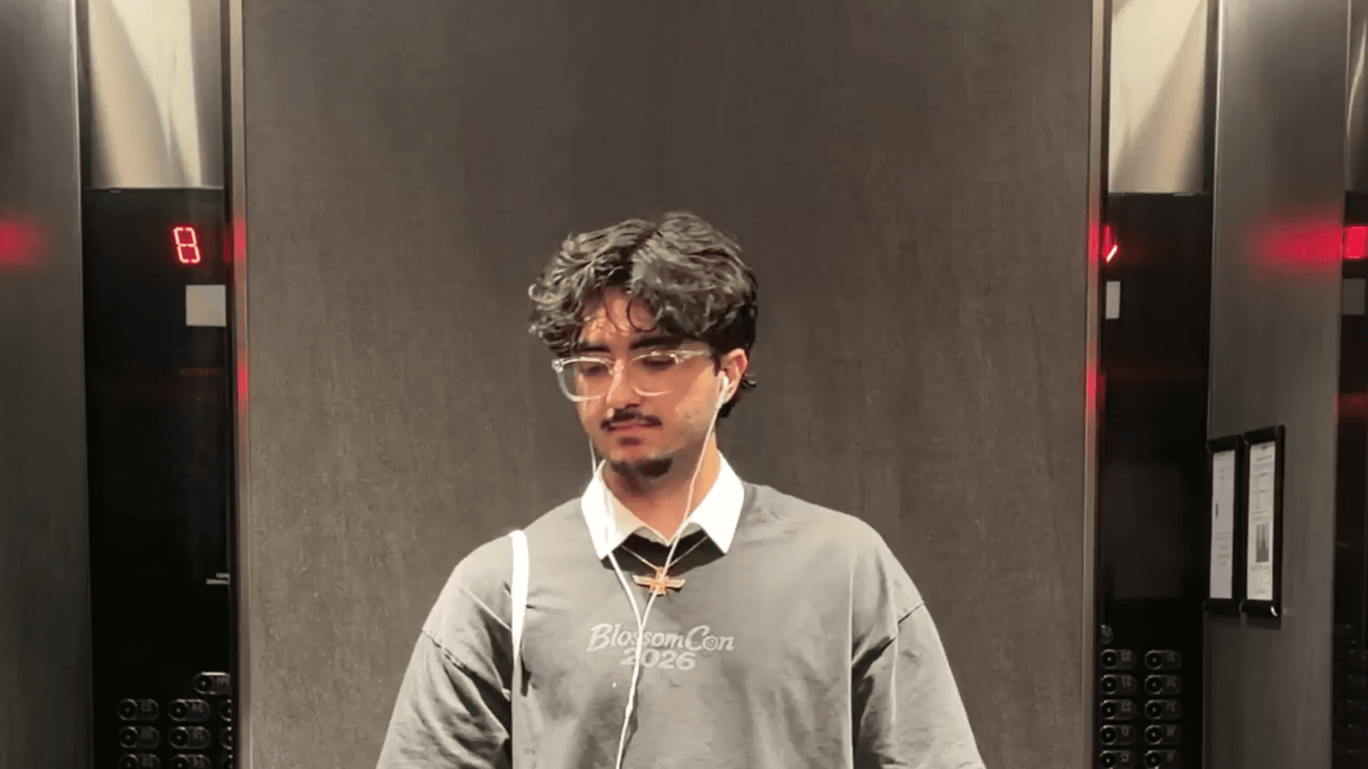 Radin in an elevator wearing a BlossomCon 2026 shirt, from the application film